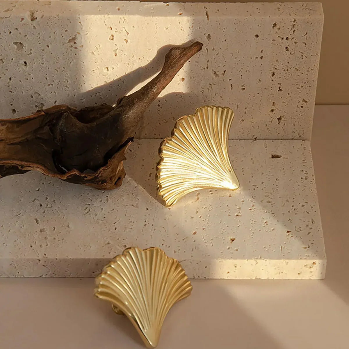 Gold shell-shaped objects on a textured stone surface with a piece of driftwood.