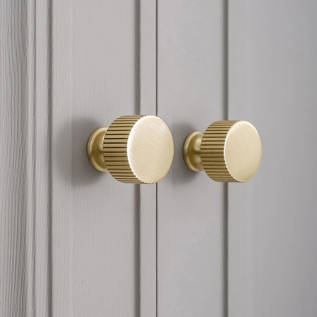 Brass Essence linear knurled brass cabinet knob with a textured surface and polished finish, mounted on a wooden cabinet door.