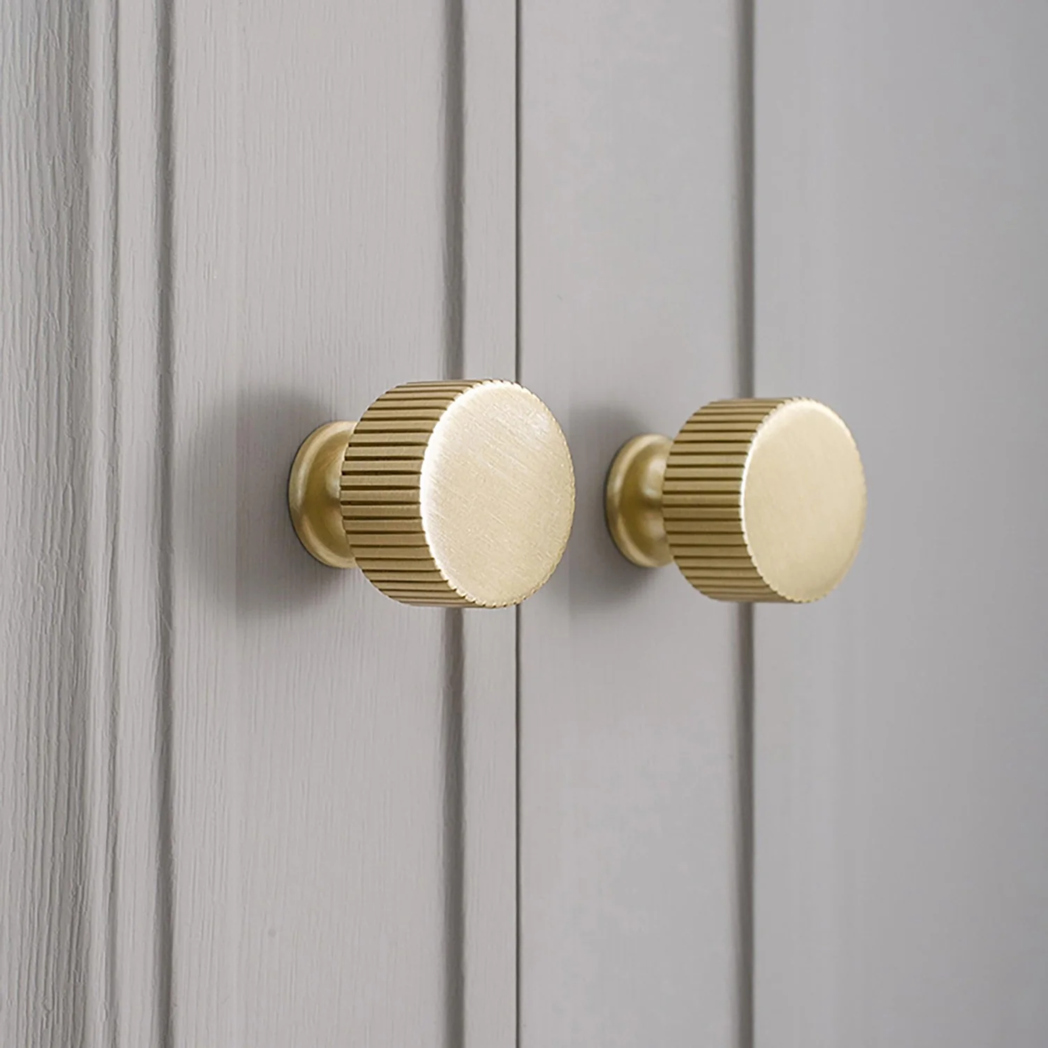Brass Essence linear knurled brass cabinet knob with a textured surface and polished finish, mounted on a wooden cabinet door.
