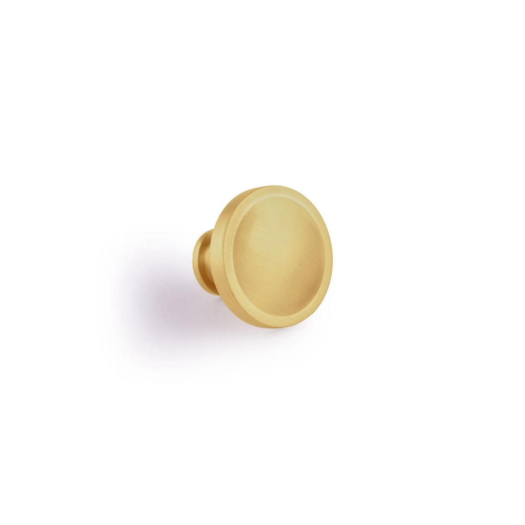 Brass essence Krisha brushed brass round cabinet knob with smooth finish and modern design, shown in close-up image.