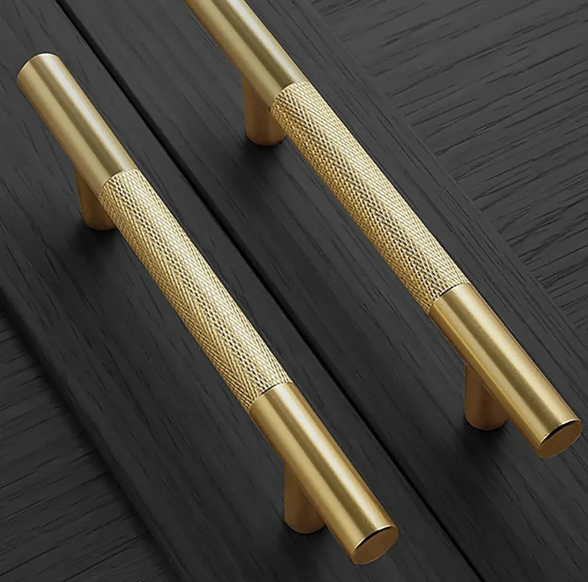 Two gold cabinet handles on a dark wooden surface